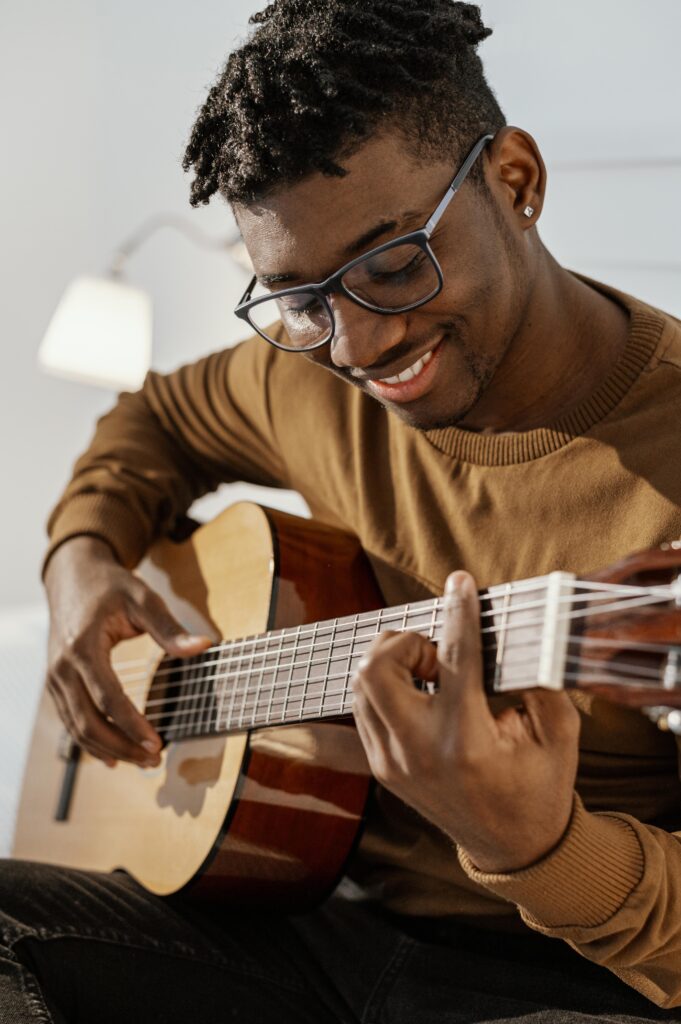 front-view-smiley-male-musician-home-playing-guitar-bed